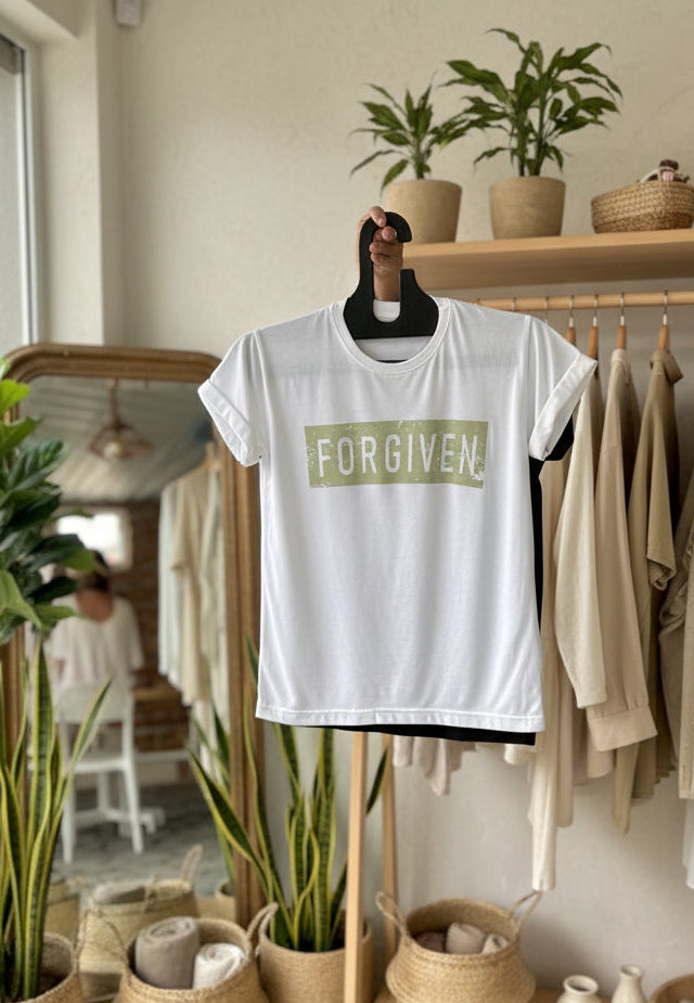 White t-shirt with 'FORGIVEN' printed on it, held up on a hanger in an indoor setting.