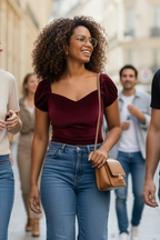 Woman walking outdoors wearing a burgundy top and blue jeans, holding a brown handbag.