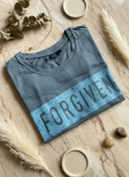 Folded blue shirt with 'FORGIVEN' text on a textured surface