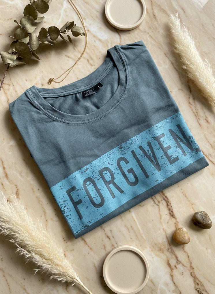 Folded blue shirt with 'FORGIVEN' text on a textured surface