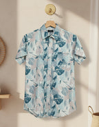 Short-sleeve shirt with a floral pattern hanging on a wooden hanger against a neutral wall.