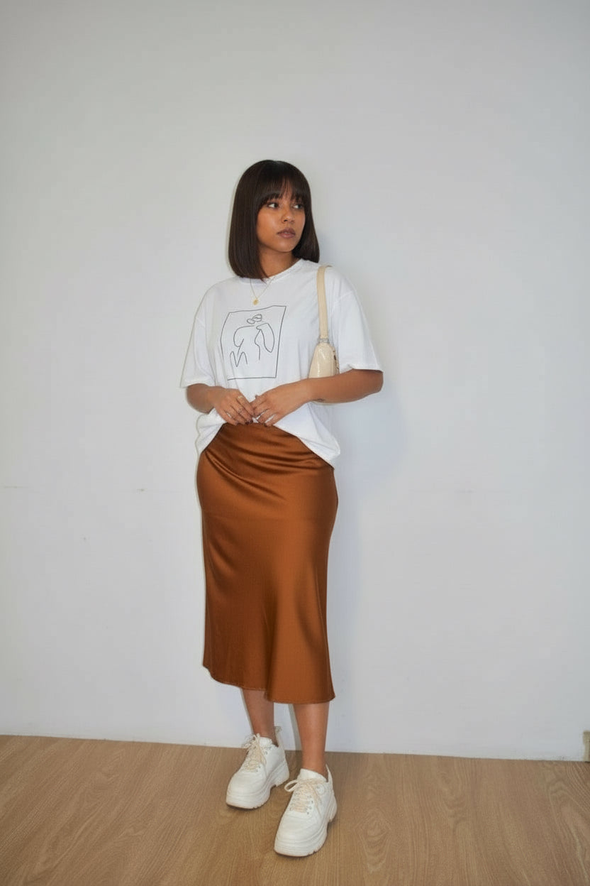 Woman wearing a white t-shirt, brown satin skirt, and white sneakers against a plain background