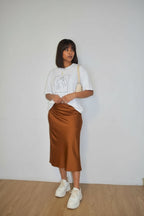 Woman wearing a white t-shirt, brown satin skirt, and white sneakers against a plain background
