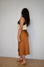 Woman wearing a brown skirt and navy top against a white wall