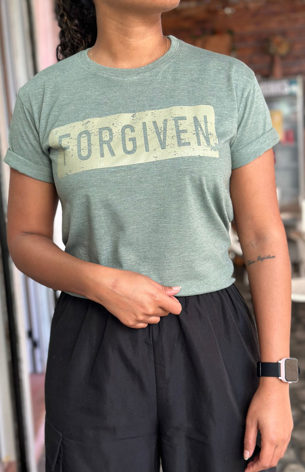 Person wearing a green t-shirt with 'FORGIVEN' printed on it, standing indoors.