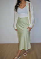 Person wearing a light green skirt, white top, and cream cardigan against a plain background
