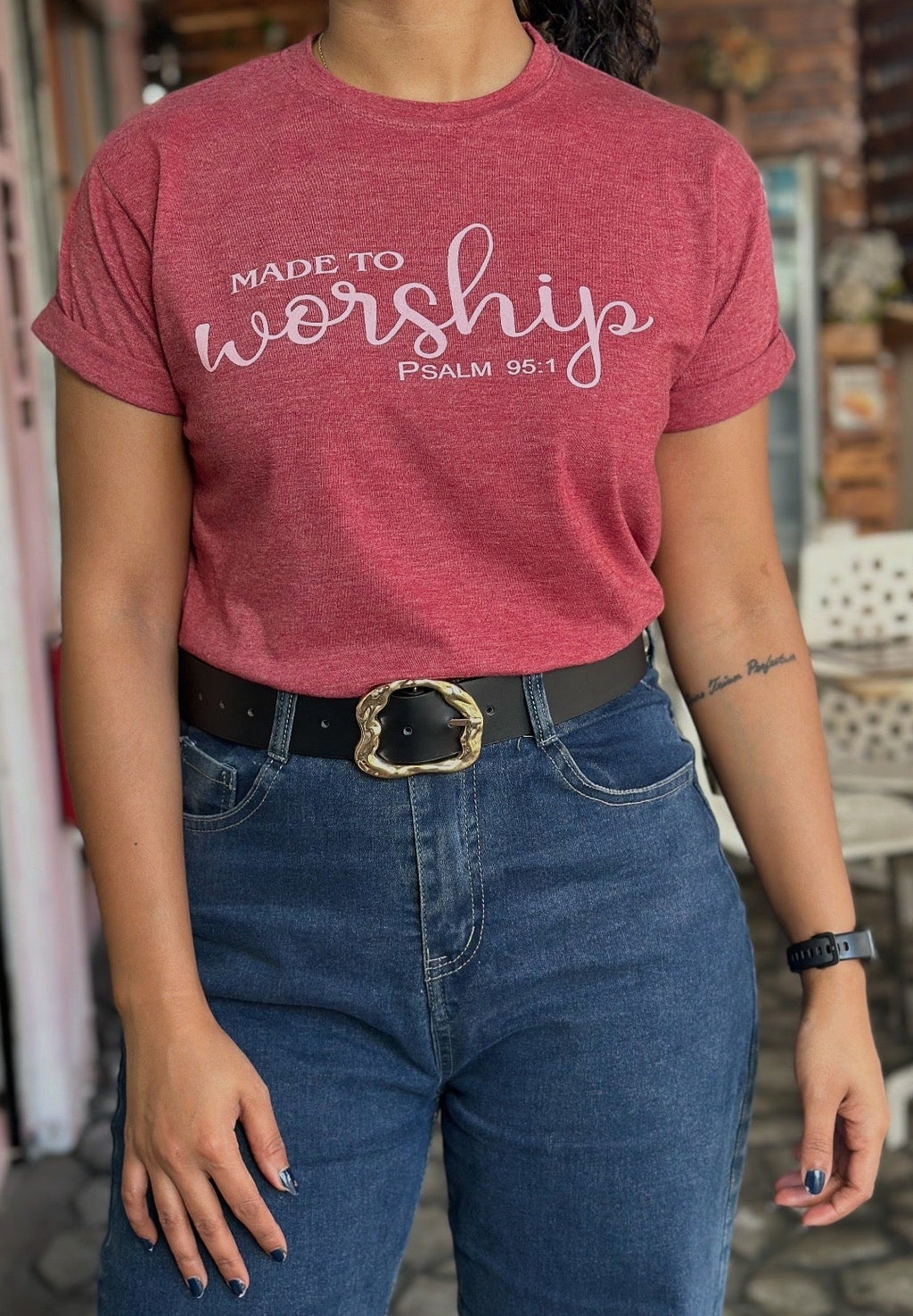 Person wearing a red t-shirt with 'Made to Worship' text, standing outdoors.