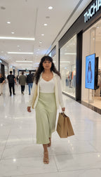 Woman walking through a shopping mall wearing a white top and light green skirt.