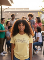 Yellow t-shirt with 'Made to worship' text on a hanger indoors.