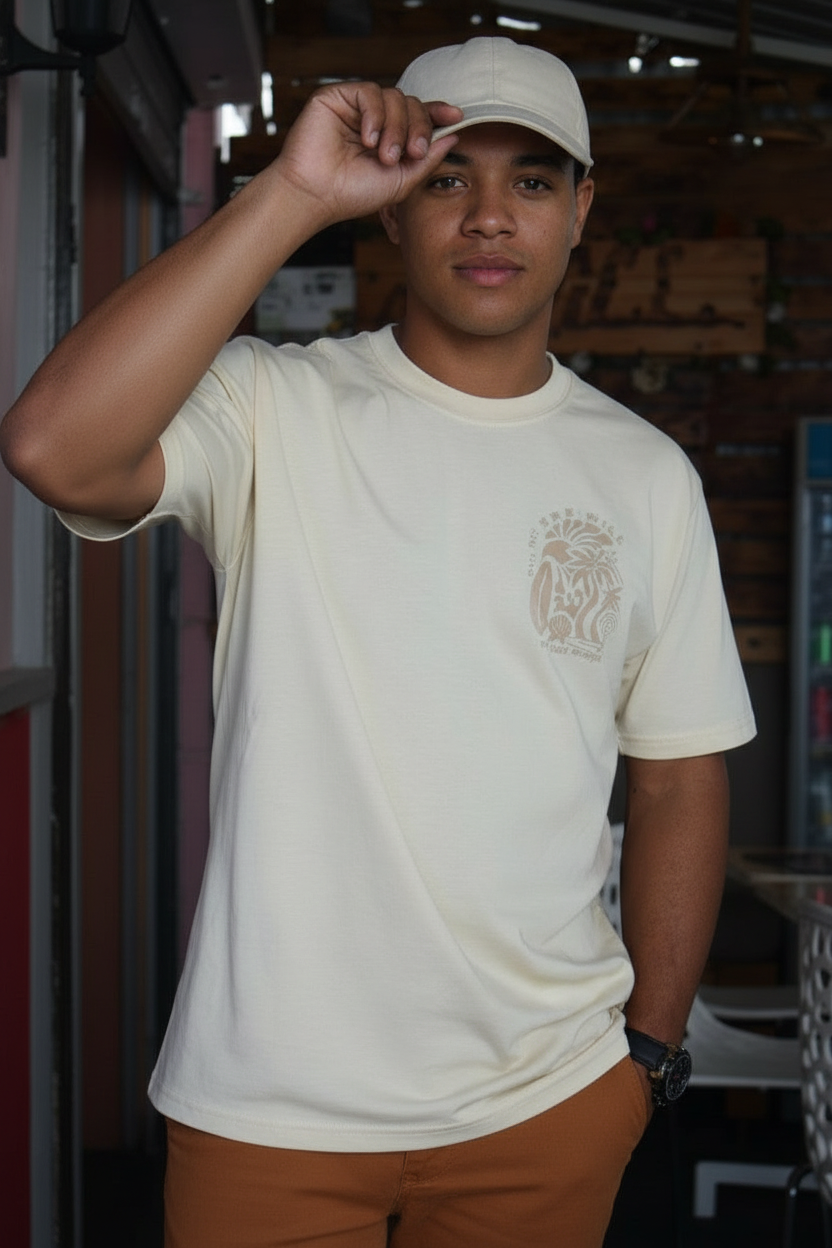 Person wearing a beige t-shirt with a logo and brown pants, standing indoors.