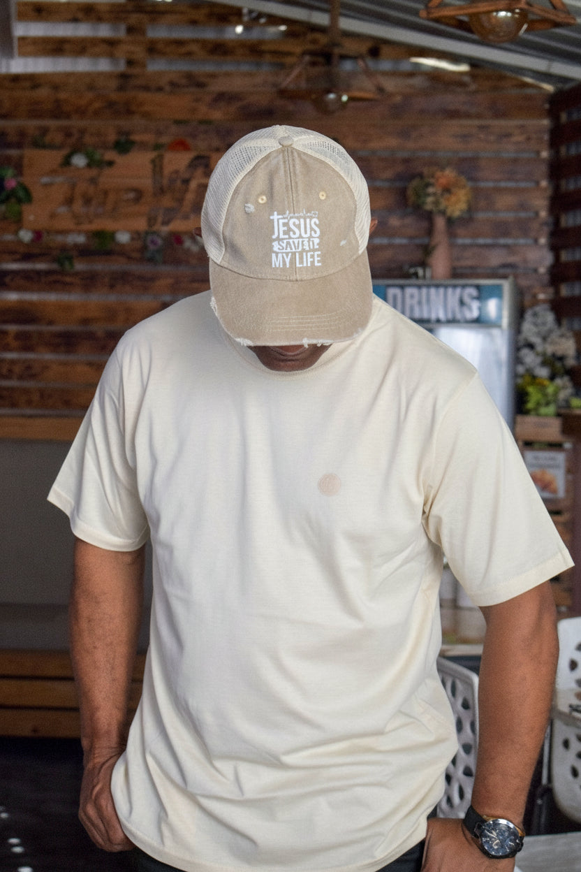 Person wearing a beige cap with text and a white t-shirt in an indoor setting.