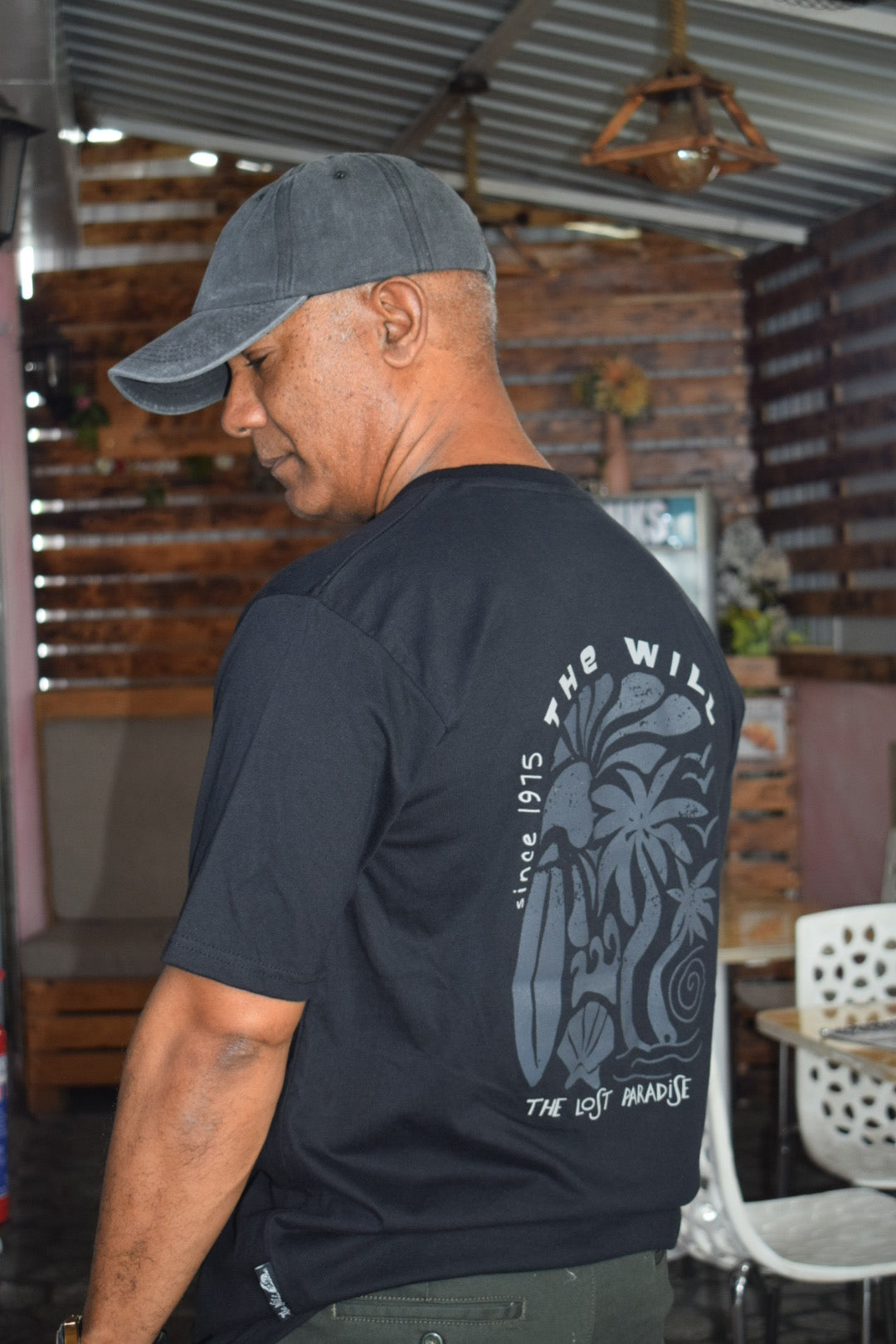 Man wearing a black t-shirt with a logo and text, bending over in an outdoor setting.