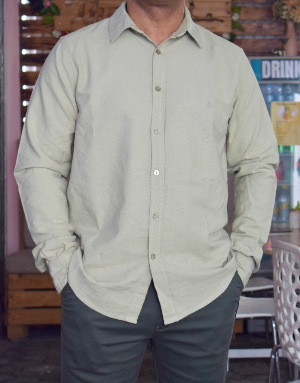Person wearing a light green button-up shirt and dark pants in an indoor setting.