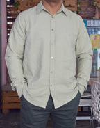 Person wearing a light green button-up shirt and dark pants in an indoor setting.