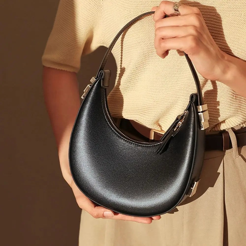 Person holding a black handbag with a neutral background