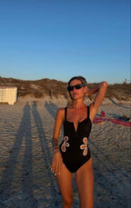 Woman in a black swimsuit with floral designs on a sandy beach.