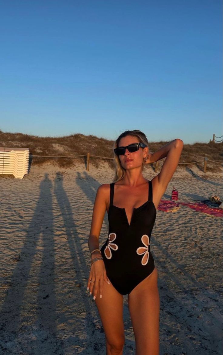 Woman in a black swimsuit with floral designs on a sandy beach.