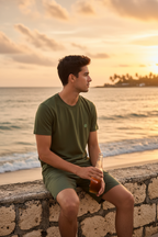 Man sitting by the ocean wearing olive green logo tee